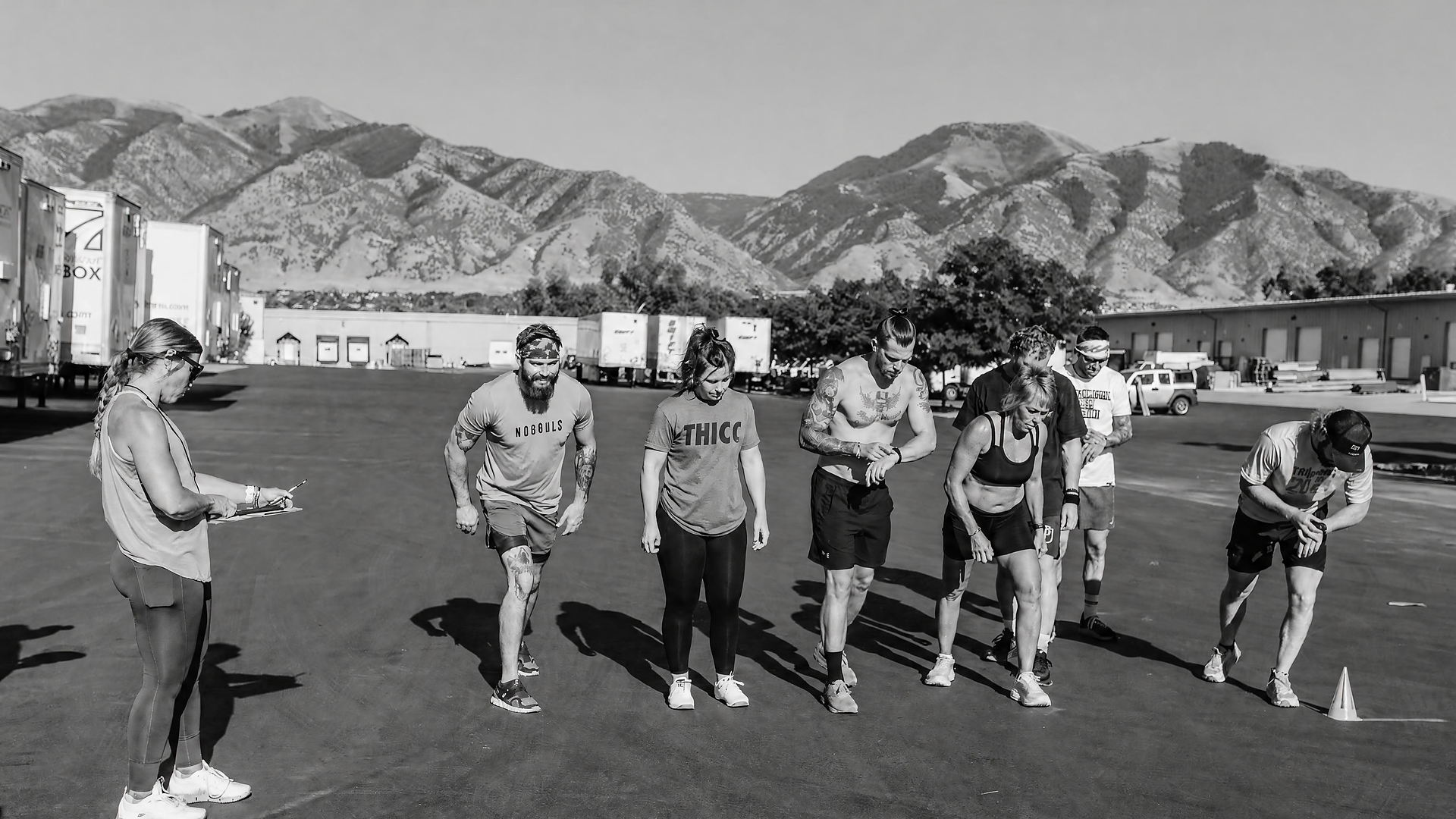 A coach with a clipboard and a line of athletes on the asphalt outside CrossFit Antietam, mountains behind them